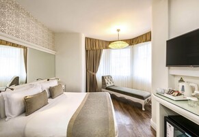A hotel room with a large bed, a bedside table with a TV, a chair, and a desk with a coffee maker.