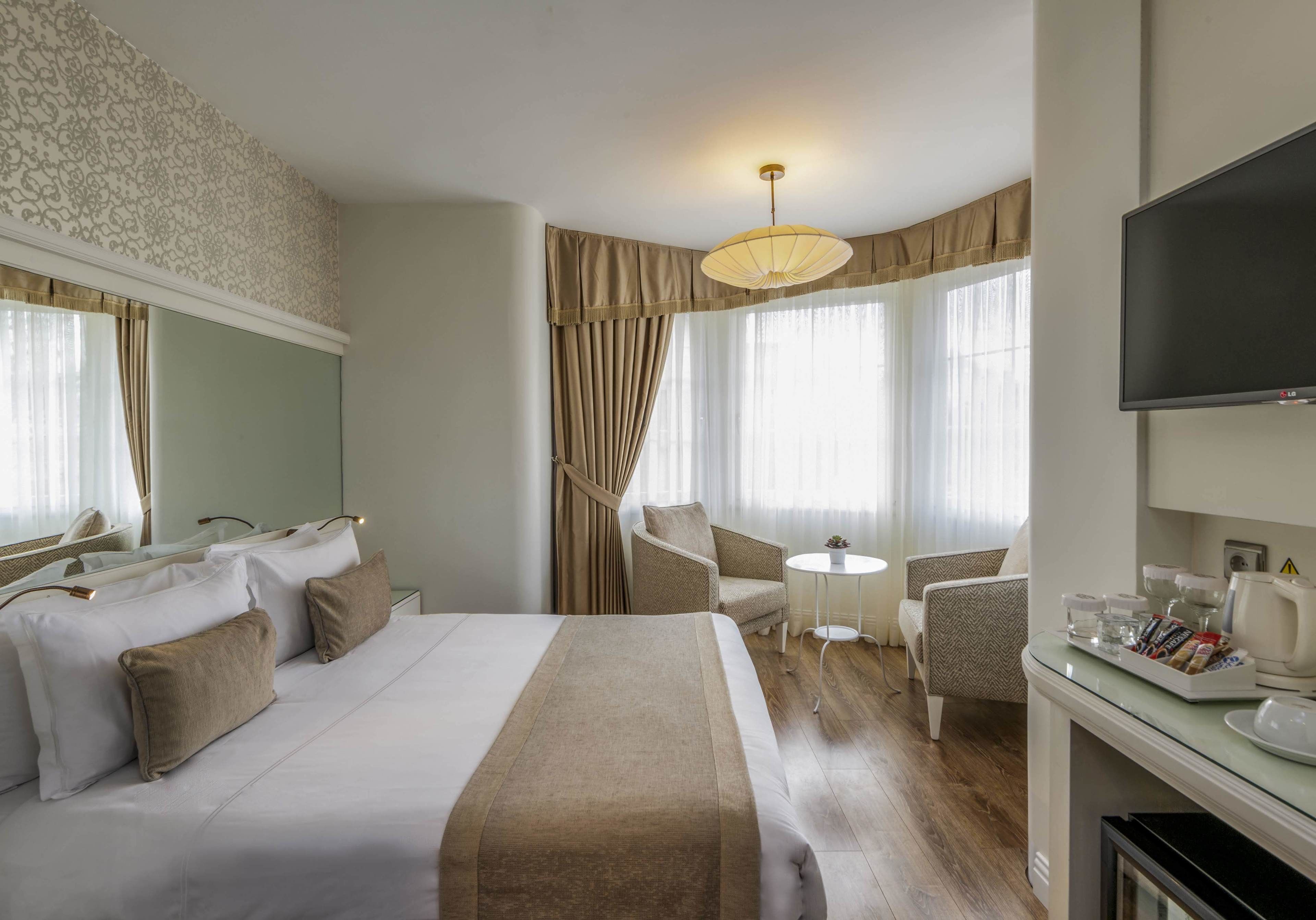 A hotel room with a large bed, a desk with a flat-screen TV, a small round table, and a chair.