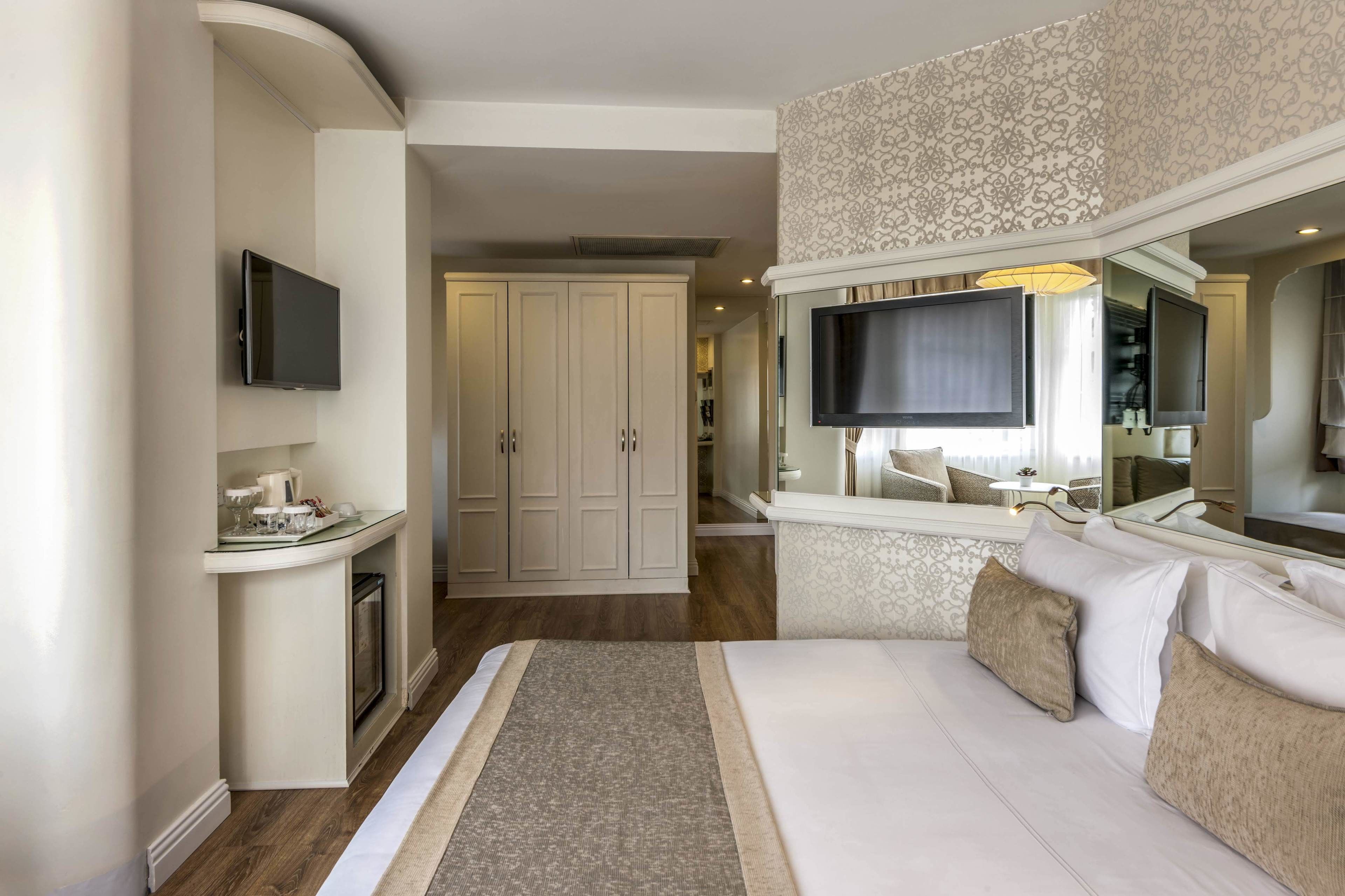 Habitación de hotel con una cama grande, un televisor montado en la pared, un armario y una pequeña zona de estar con una mesa y sillas.