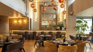A restaurant with multiple dining tables and chairs, a bar area, and hanging spherical light fixtures.