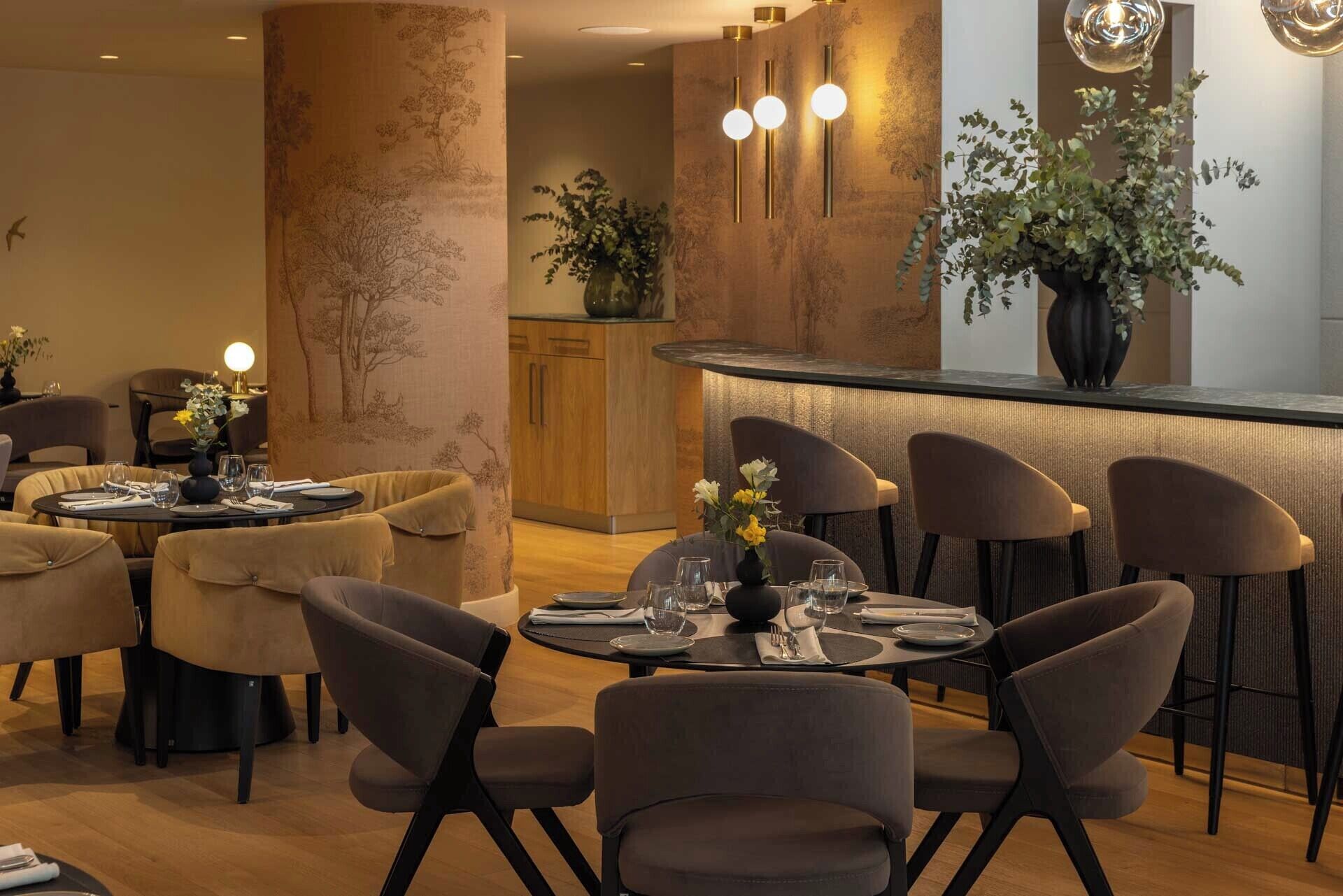 A modern dining area with round tables, cushioned chairs, and pendant lighting.