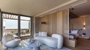 A modern hotel room with a curved sofa, a round coffee table, a bed with a headboard, and a view of the outdoors.