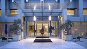 A modern hotel entrance with a glass facade, a welcoming entrance, and potted plants.