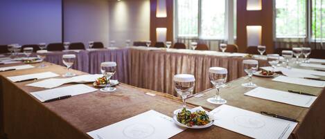 A conference room with a long table set for a meeting, equipped with chairs, wine glasses, and documents.