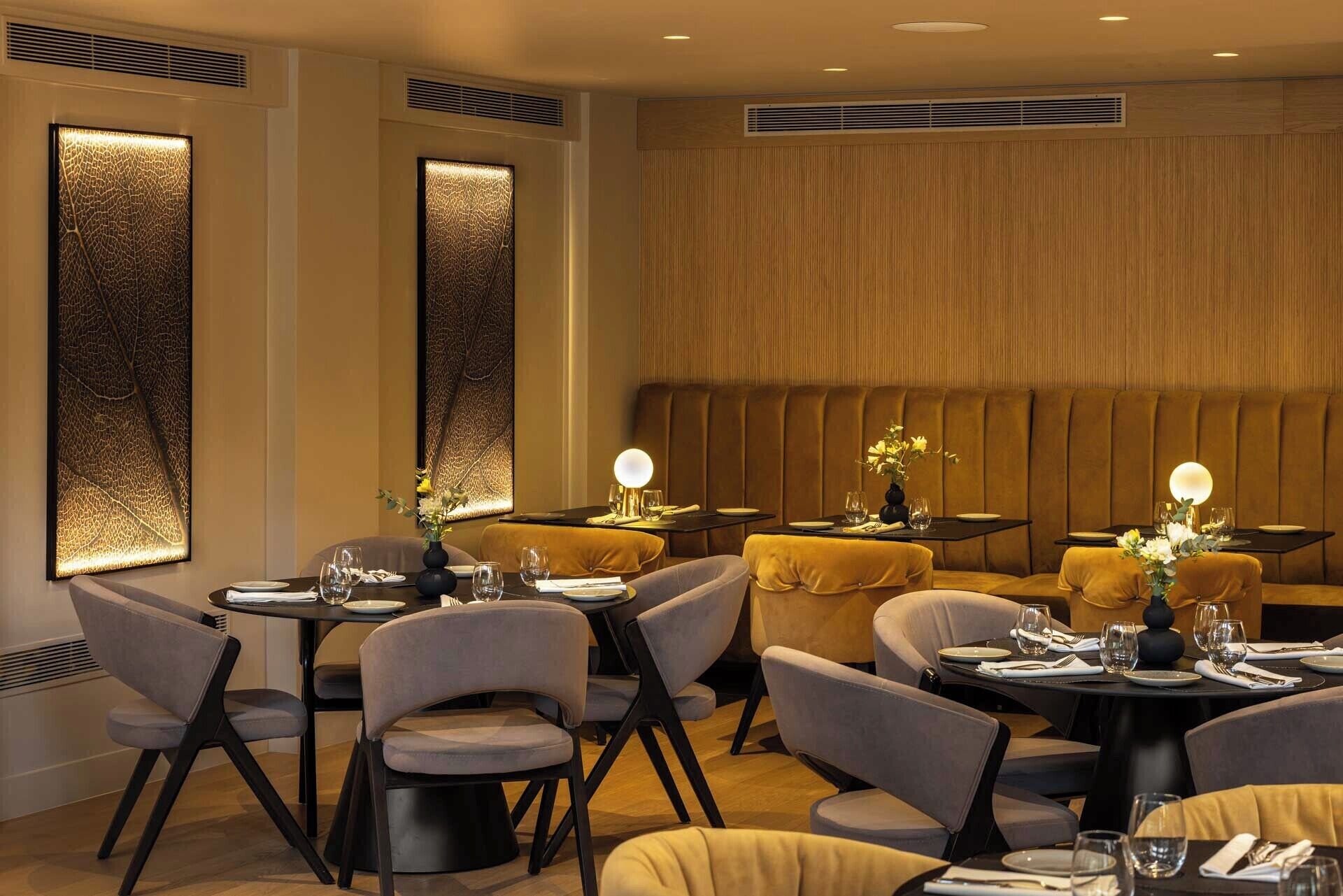 A restaurant with booths and tables, each with a vase of flowers and a lit lamp.