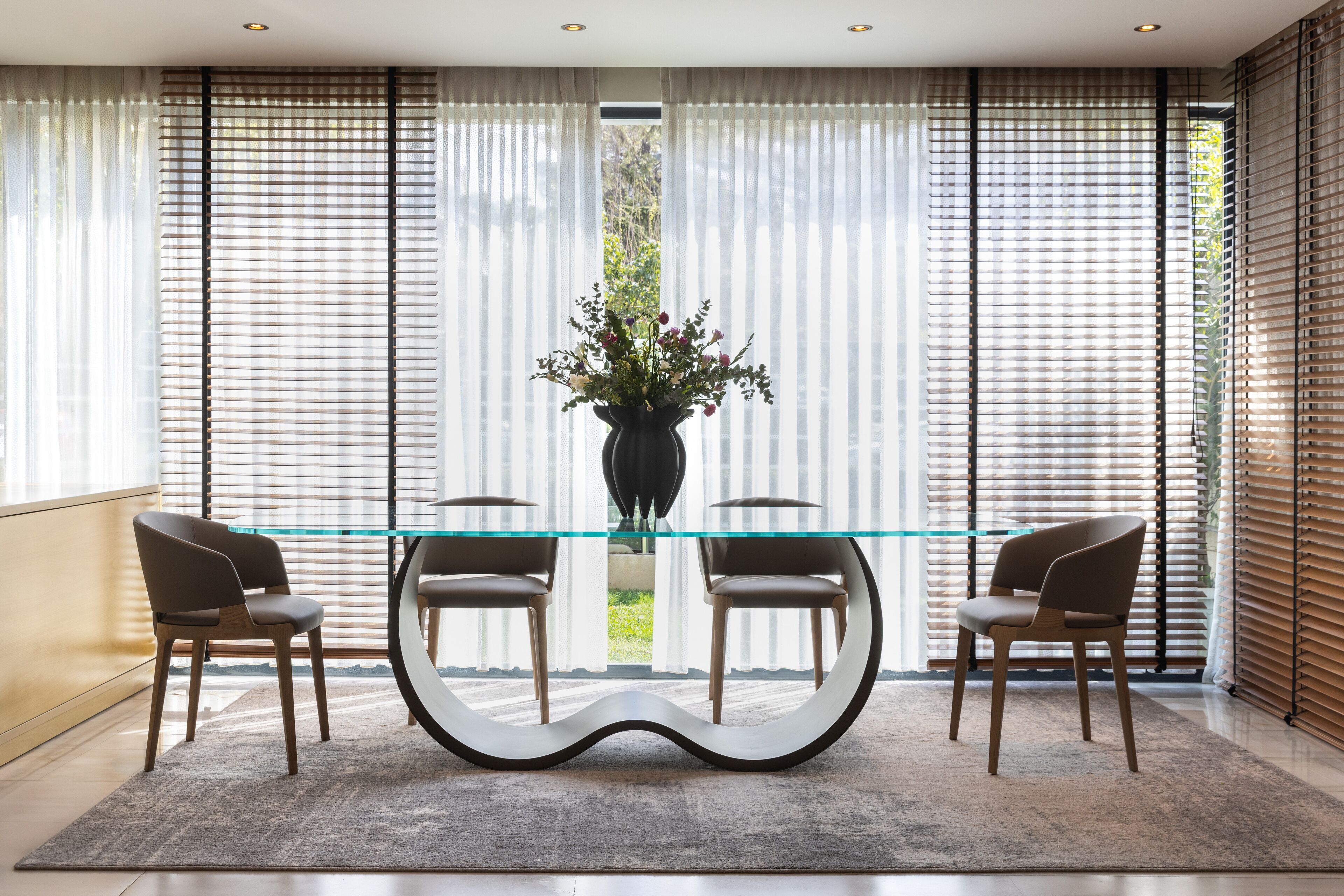 A modern dining area with a glass table, two chairs, and a vase of flowers.