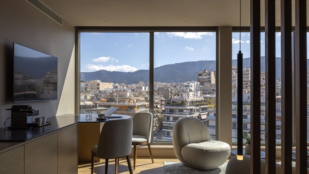 A modern room with a large window, a flat-screen TV, a desk, two chairs, and a sofa.