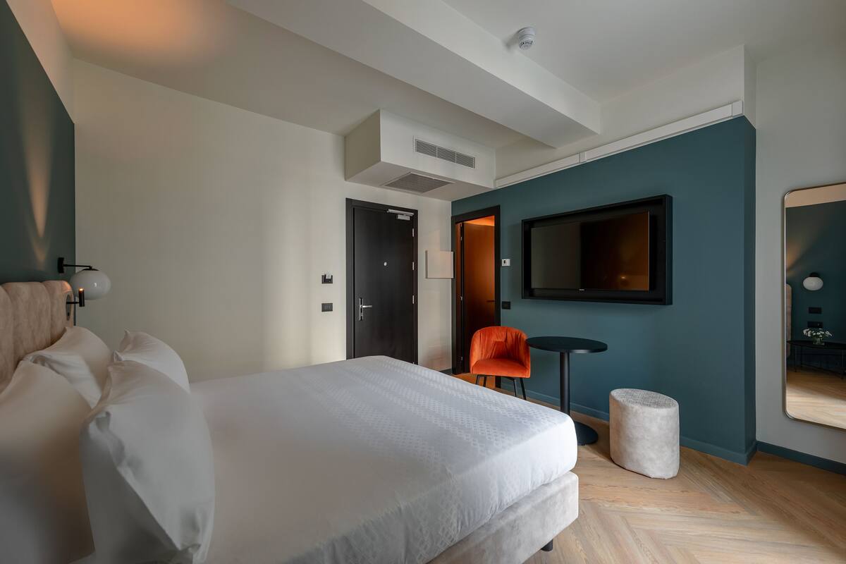 A modern hotel room with a large bed, a small table, a chair, and a television.