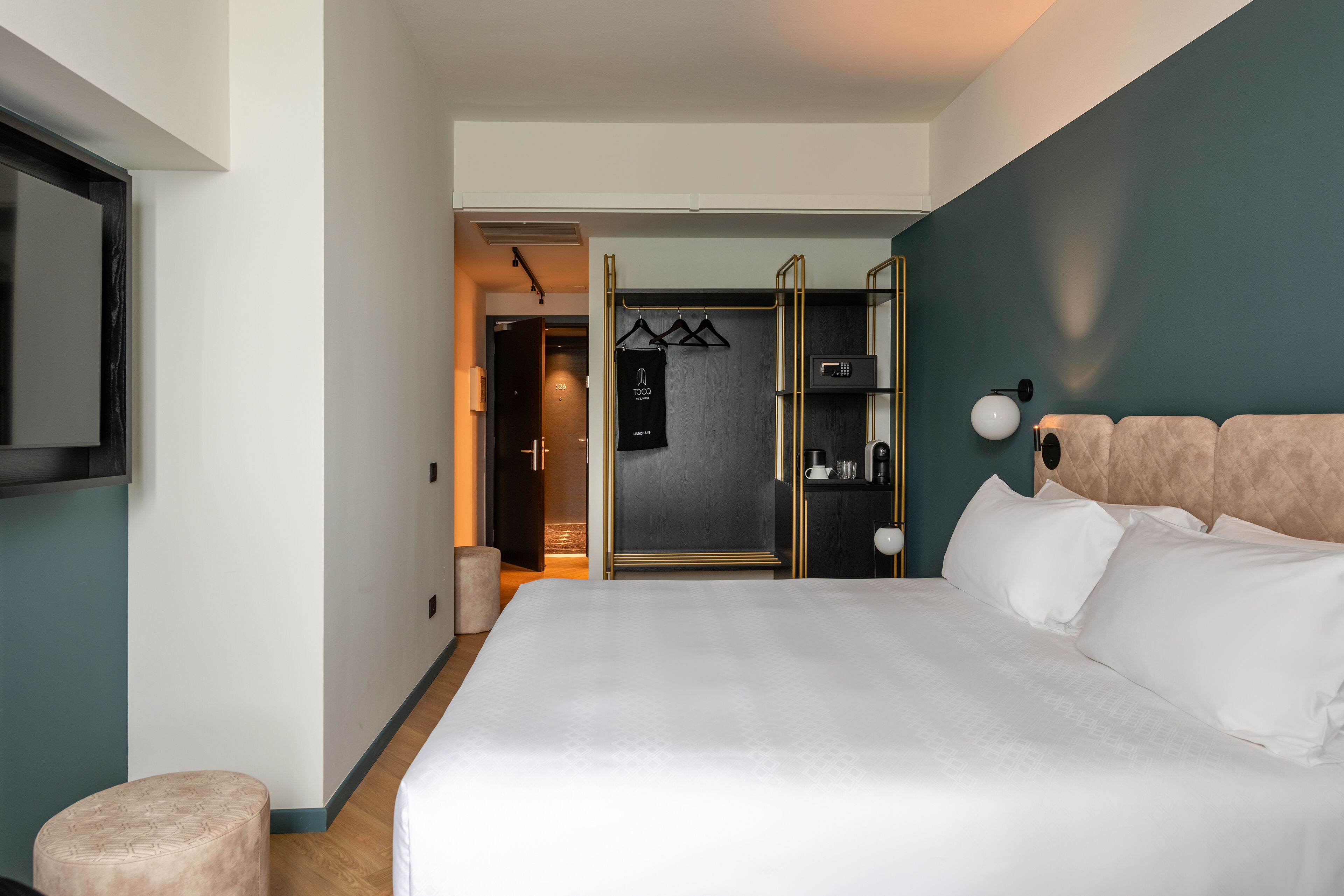 A modern hotel room with a large bed, a wardrobe with a mirror, and a seating area with a small table and chair.