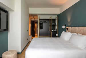 Una camera d'albergo moderna con un letto grande, un armadio con specchio e un angolo salotto con un tavolino e una sedia.