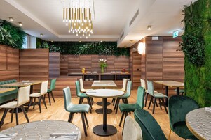Een modern restaurantinterieur met houten lambrisering, groen gestoffeerde stoelen en een ronde centrale tafel.