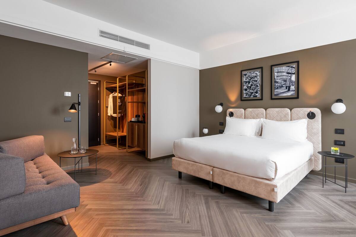 A modern hotel room with a large bed, a seating area, and a walk-in closet.
