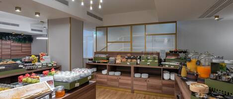 A modern breakfast buffet with various food items and beverages, wooden flooring, and contemporary lighting fixtures.