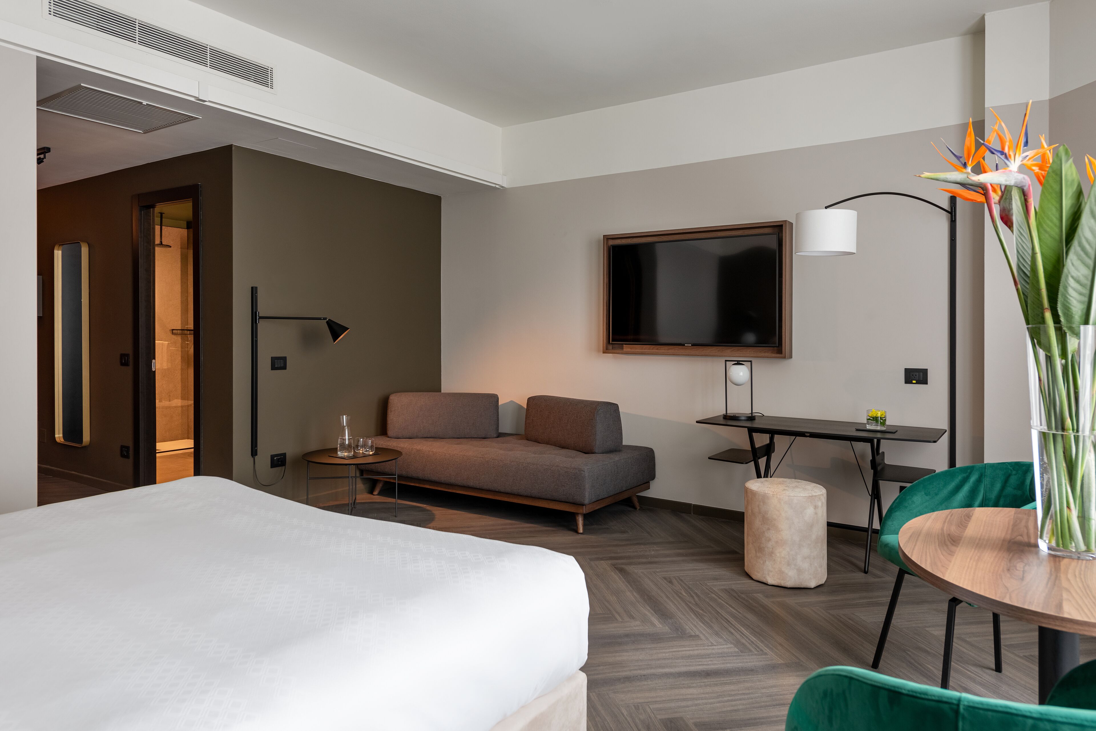 Ein modernes Hotelzimmer mit einem großen Bett, einer Couch, einem kleinen Tisch, einem Fernseher und einer Pflanze.