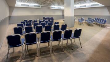 Un salón de conferencias con filas de sillas azules, un techo alto con tragaluces y una decoración en tonos neutros.