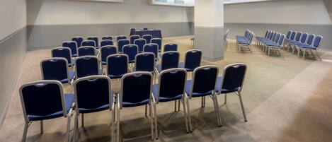 A conference room with rows of blue chairs, a high ceiling with skylights, and a neutral color scheme.