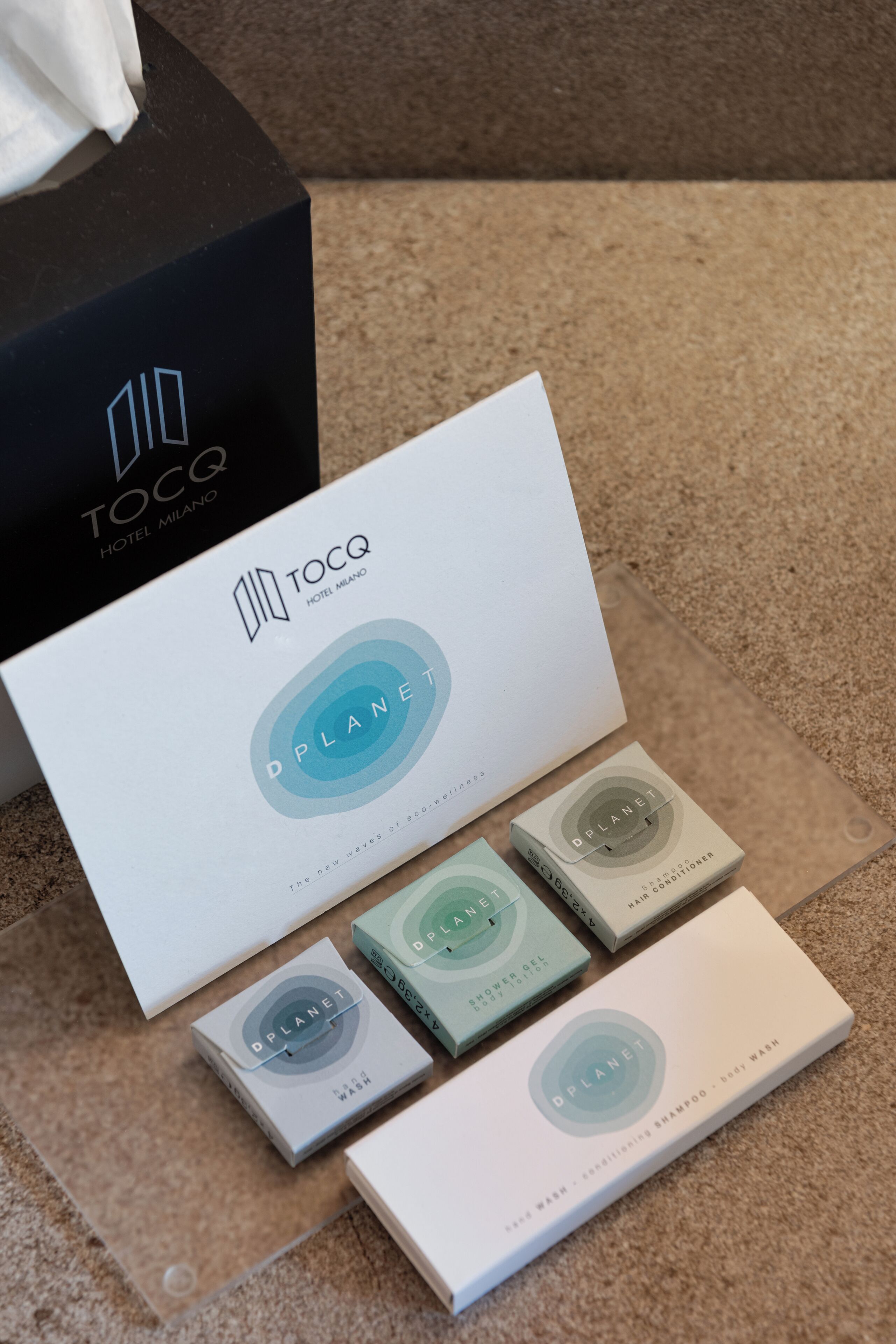 A hotel package with a TOCQ Hotel Milano branded box and DPLANET branded toiletries.