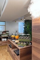 A modern kitchen with wooden cabinets, a coffee station, and a green wall with a plant.