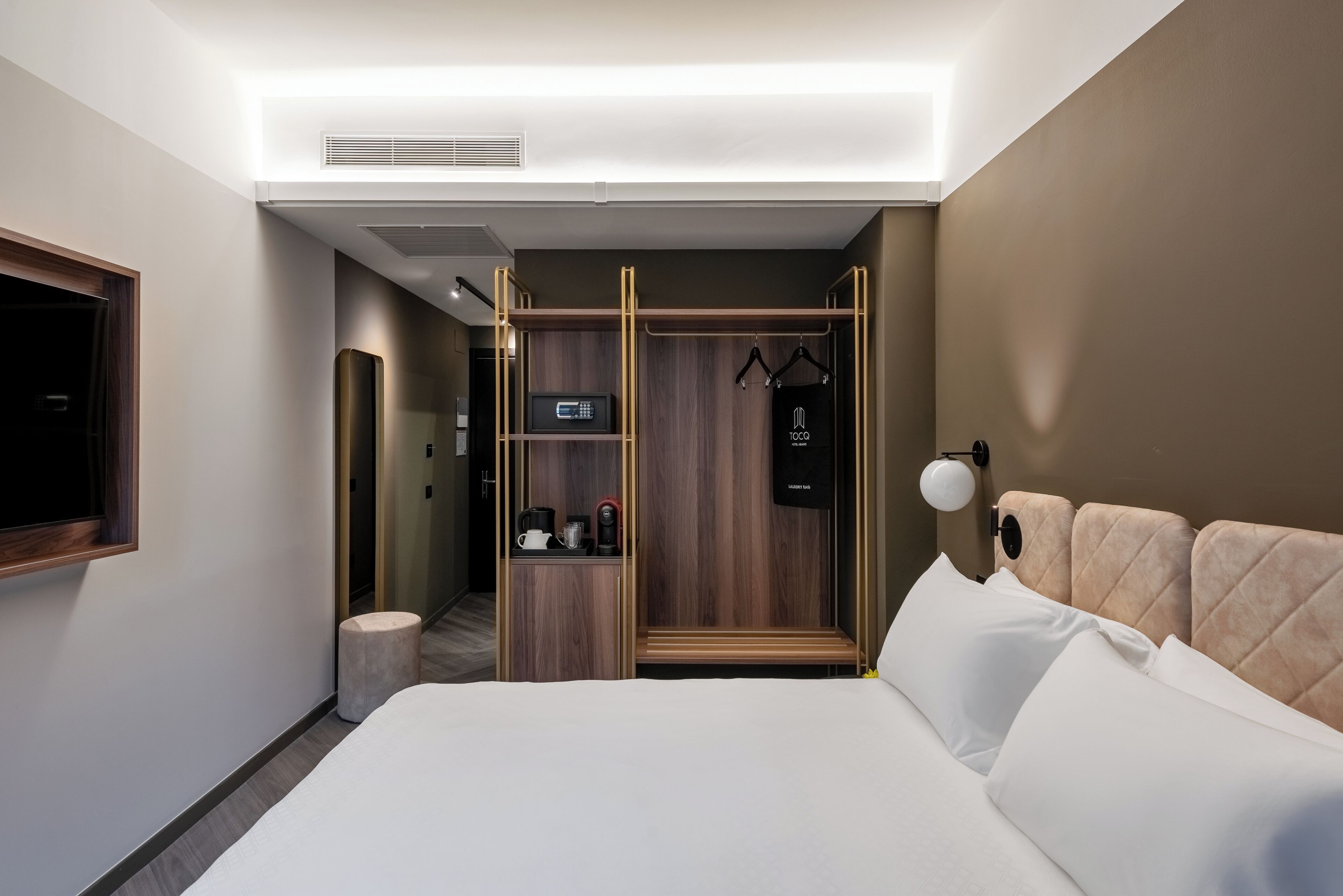 Una habitación de hotel moderna con cama, armario, televisor y una pequeña zona de estar.