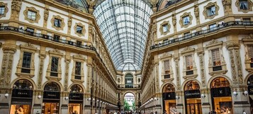 A grand, ornate building with a glass dome ceiling and multiple luxury brand stores on either side.