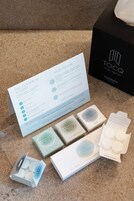 A product display with a booklet titled 'HOW TO USE,' a black box labeled 'TOCQ HOTEL MILANO,' and various items including a white box and a blue box with circular objects.