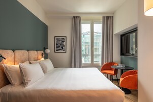 Una camera d'albergo moderna con un letto grande, un tavolino, due sedie, una TV e una finestra con tende.