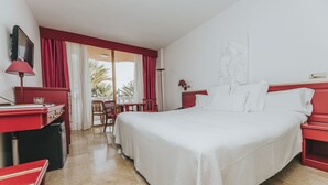 A hotel room with a large bed, a desk with a computer, a chair, and a view of palm trees through the window. - Cleopatra Palace Hotel (Arona)