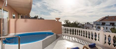 Zona de piscina al terrat amb un banyera d'hidromassatge, gandules i una barana blanca.