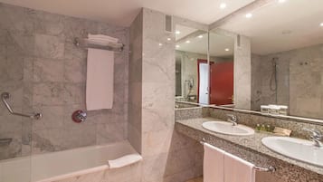 Une salle de bain moderne avec une baignoire, deux lavabos, un grand miroir et des murs en marbre.