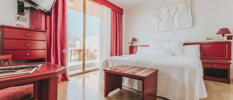 Ein Hotelzimmer mit Bett, Schreibtisch, Stuhl, Fernseher und einer Schiebetür zum Balkon.