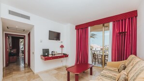 A hotel room with a sofa, a small table, a TV mounted on the wall, and a sliding glass door leading to a balcony. - Cleopatra Palace Hotel (Arona)