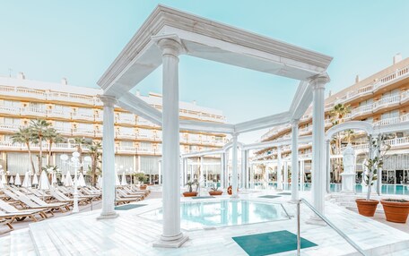 A hotel pool area with white columns, sun loungers, and a clear blue pool.