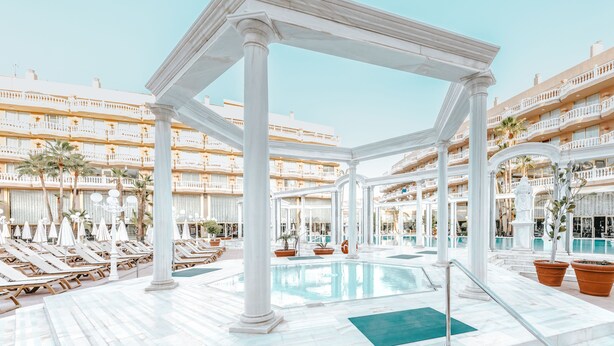 A hotel pool area with white columns, sun loungers, and a clear blue pool. - Cleopatra Palace Hotel (Arona)