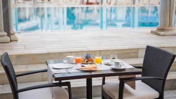 A dining table with plates, cups, and glasses, set against a poolside view.