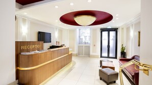 A reception area with a wooden desk, a television, and a red ceiling light. - Astor Court Hotel (London)