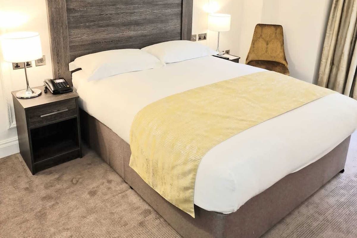 A hotel room with a large bed, two bedside tables, a lamp, and a telephone.