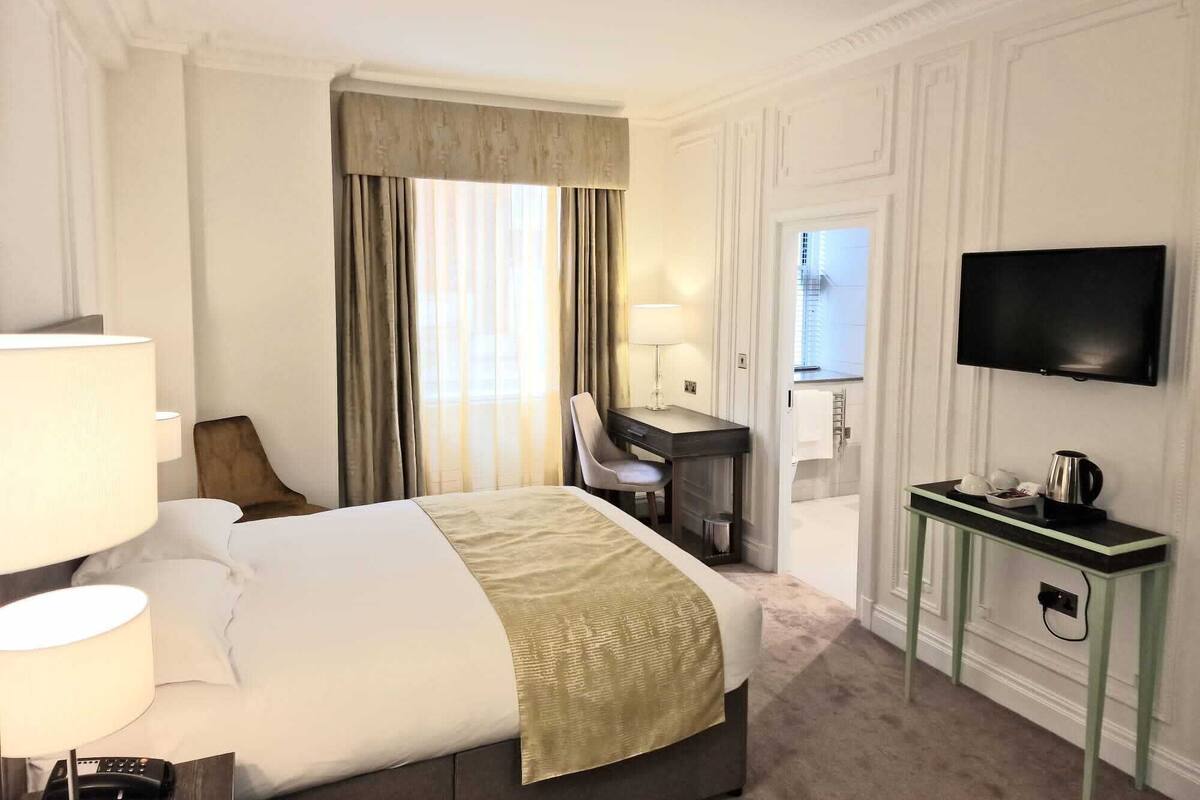A hotel room with a bed, a desk, a chair, a TV, and a coffee maker.