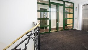 A modern hotel lobby with a carpeted floor, a staircase with a black railing, and green-framed glass doors leading to a room. - Astor Court Hotel (London)