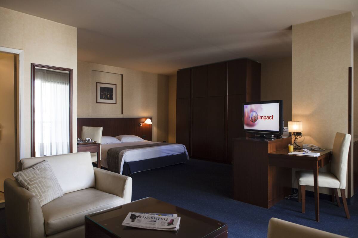 A hotel room with a bed, a sofa, a desk with a computer, and a television.