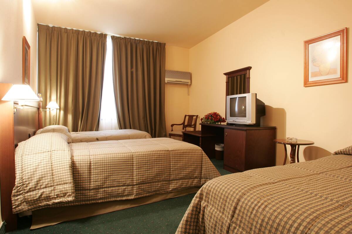 A hotel room with two beds, a desk with a television, a small table, and a chair.