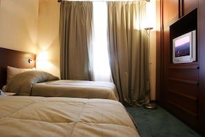 Een hotelkamer met twee bedden, een flatscreen televisie, een lamp en uitzicht op de stad.