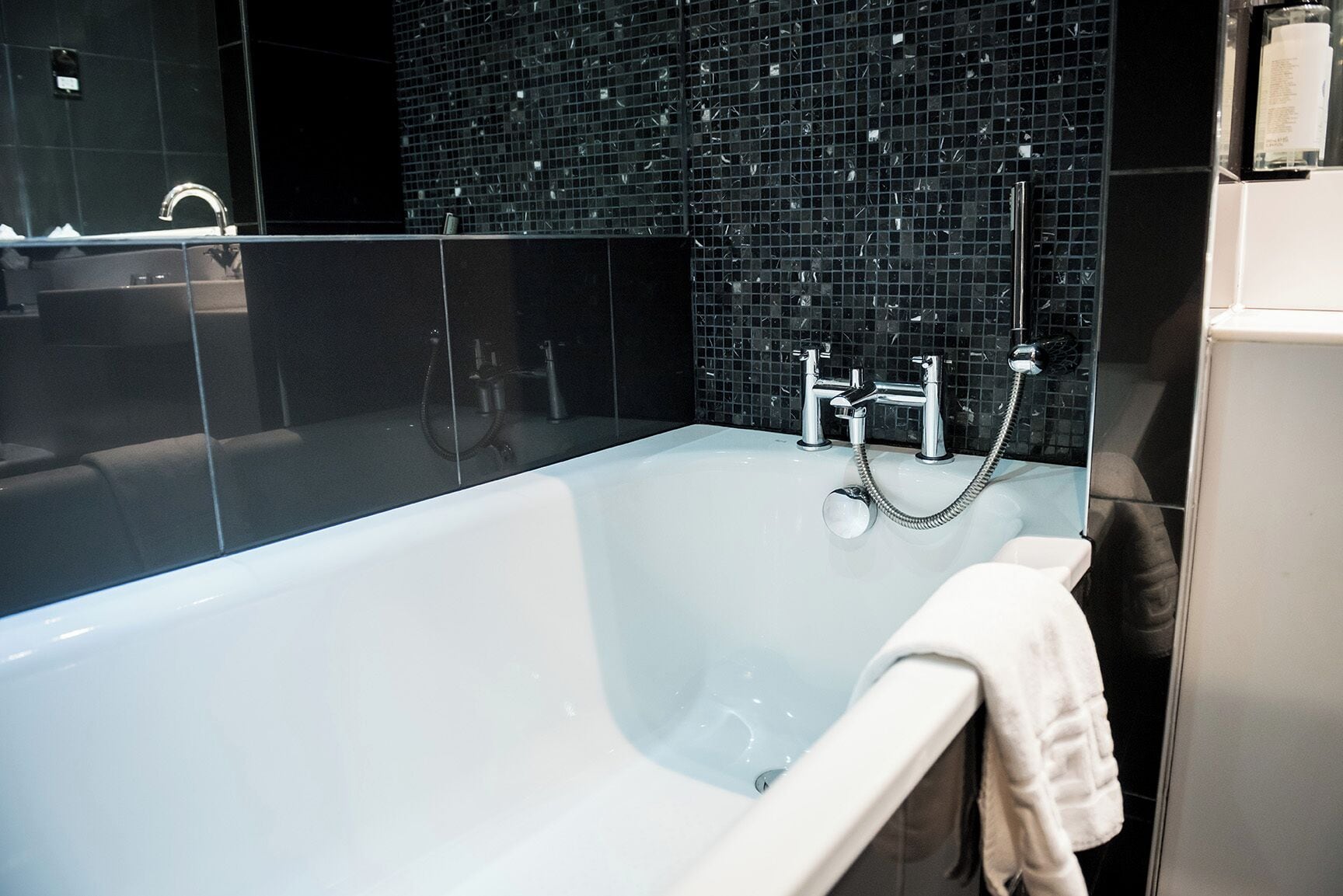 A modern bathroom with a large bathtub, a glass shower enclosure, and a black mosaic wall.