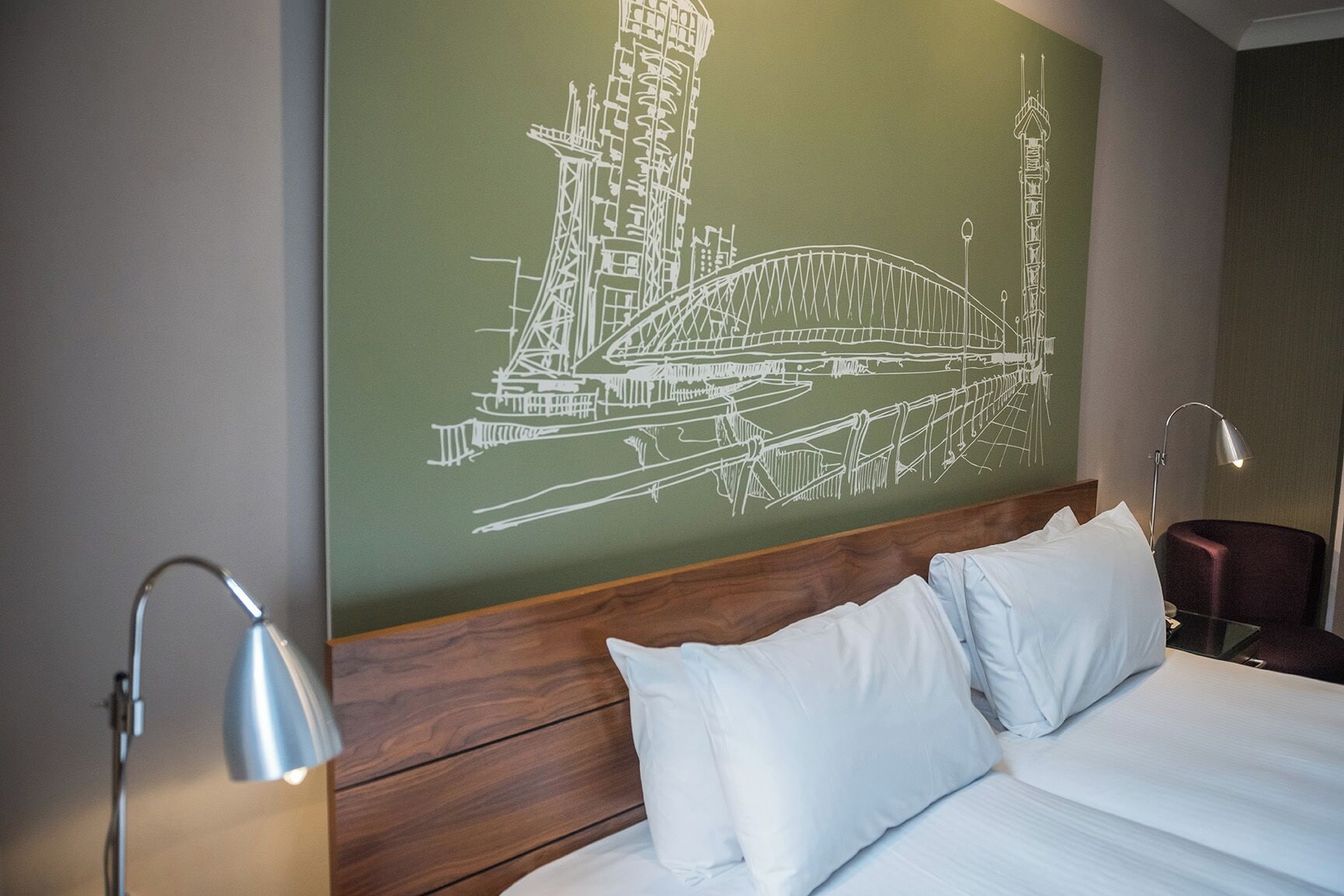 Habitación de hotel con una cama grande, dos lámparas de noche y un mural en la pared con un puente.