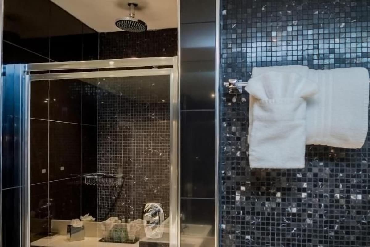 A bathroom with a glass-enclosed shower, a white towel hanging on a rack, and a tiled wall.