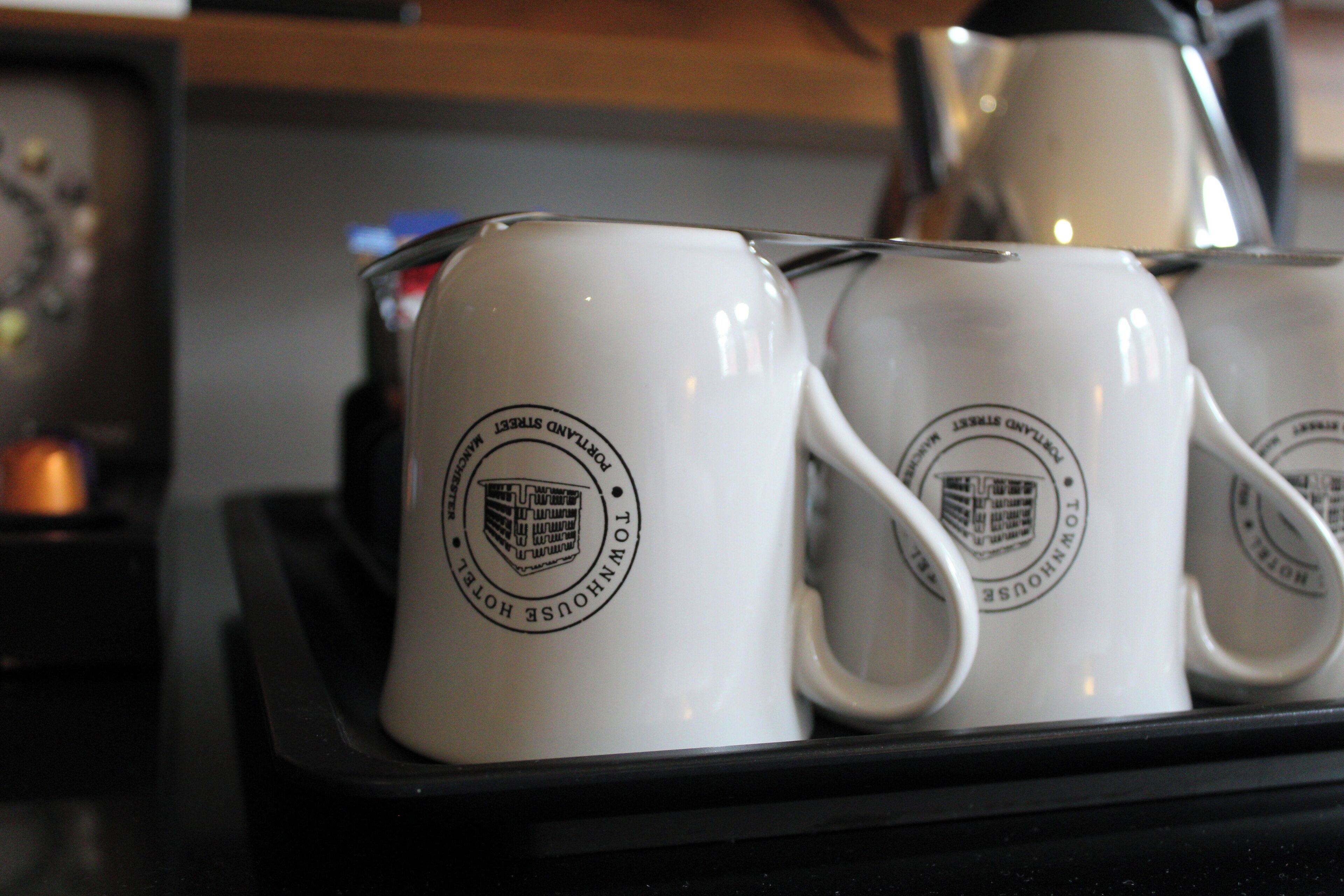 A tray with white mugs featuring a logo and text, likely indicating a hotel or establishment.