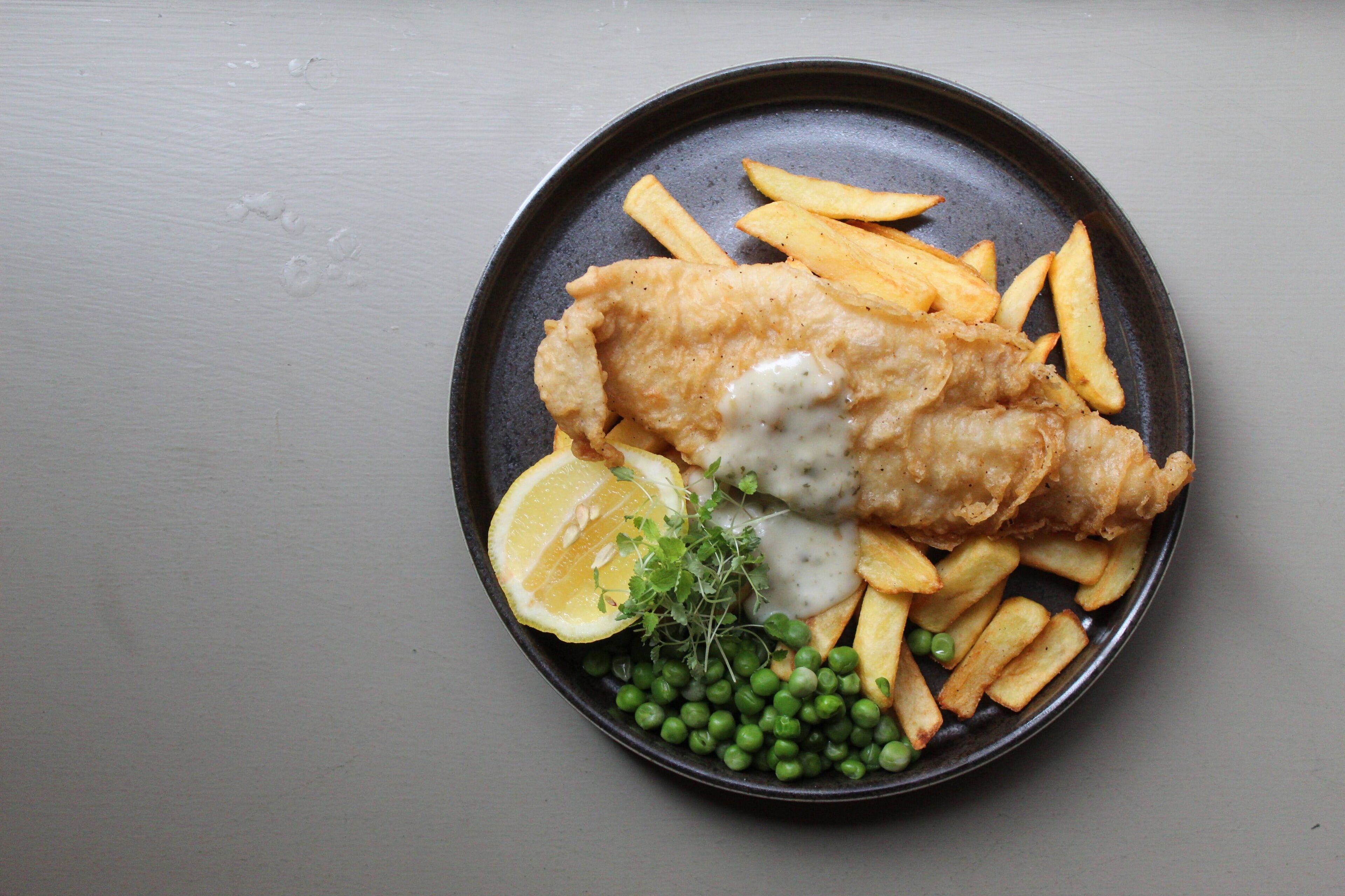 Ein Teller Fisch und Chips mit Erbsen und einem Zitronenschnitz.