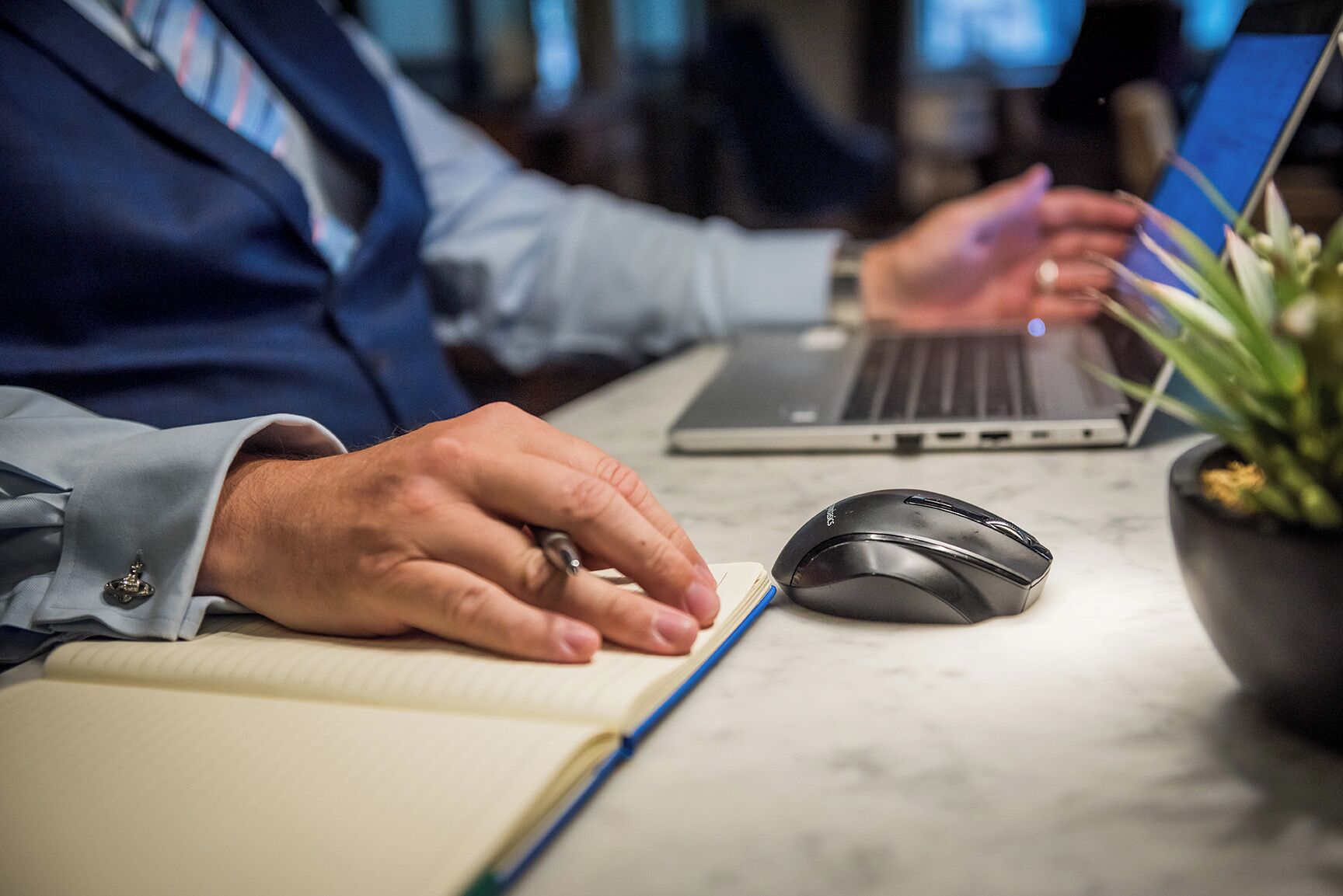 Una persona digita su un portatile con un mouse e un quaderno poggiati su una scrivania.