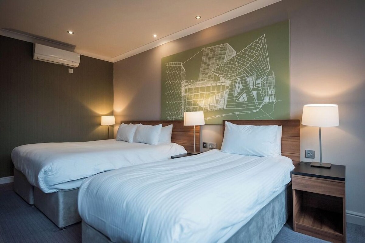 A hotel room with two beds, a wall-mounted air conditioner, and a large abstract wall art piece.