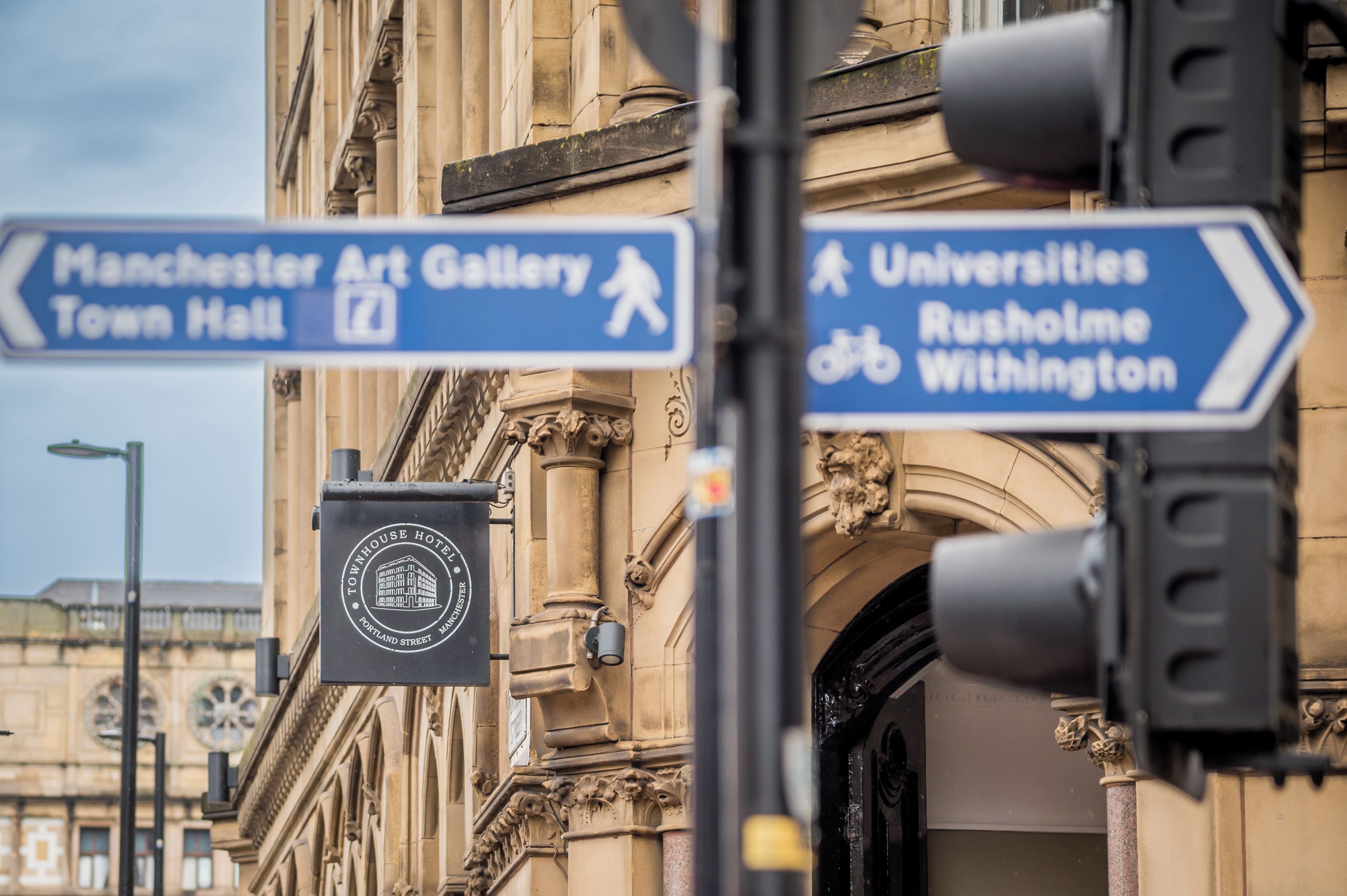 Una señal de calle con indicaciones hacia la Galería de Arte de Manchester, el Ayuntamiento y las Universidades, incluyendo Rusholme y Withington.