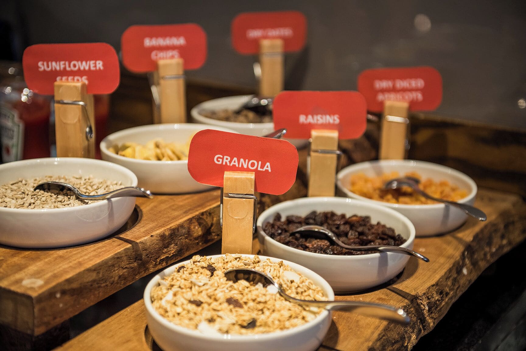 A variety of granola and dried fruit bowls on a wooden board with labels indicating different ingredients.
